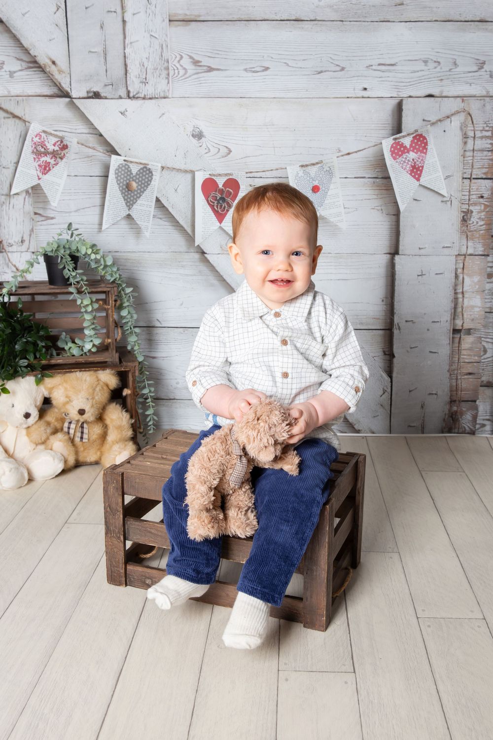 little boy holding a teddy sat on a brown crate