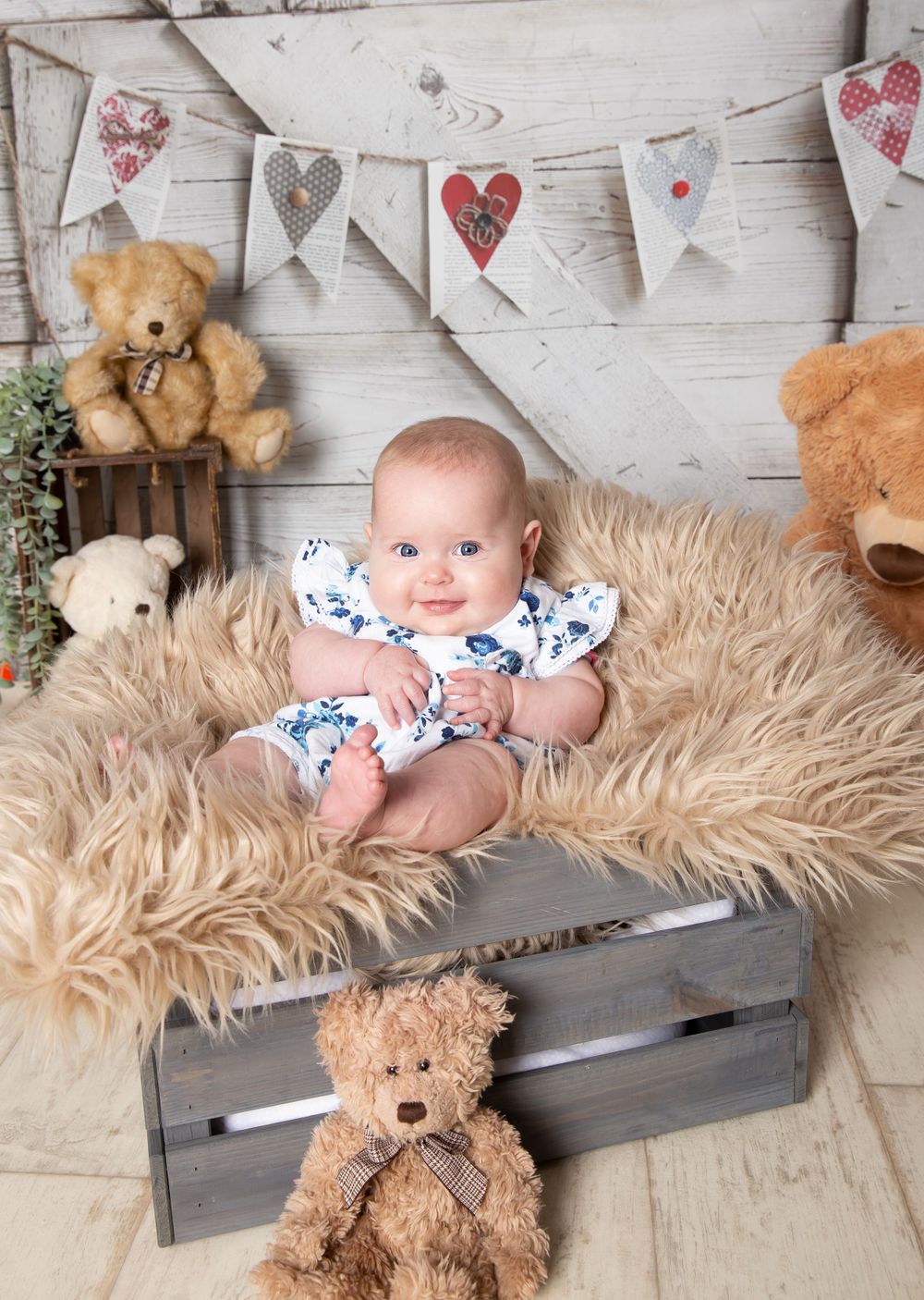 baby sat in a crate smiling with teddies