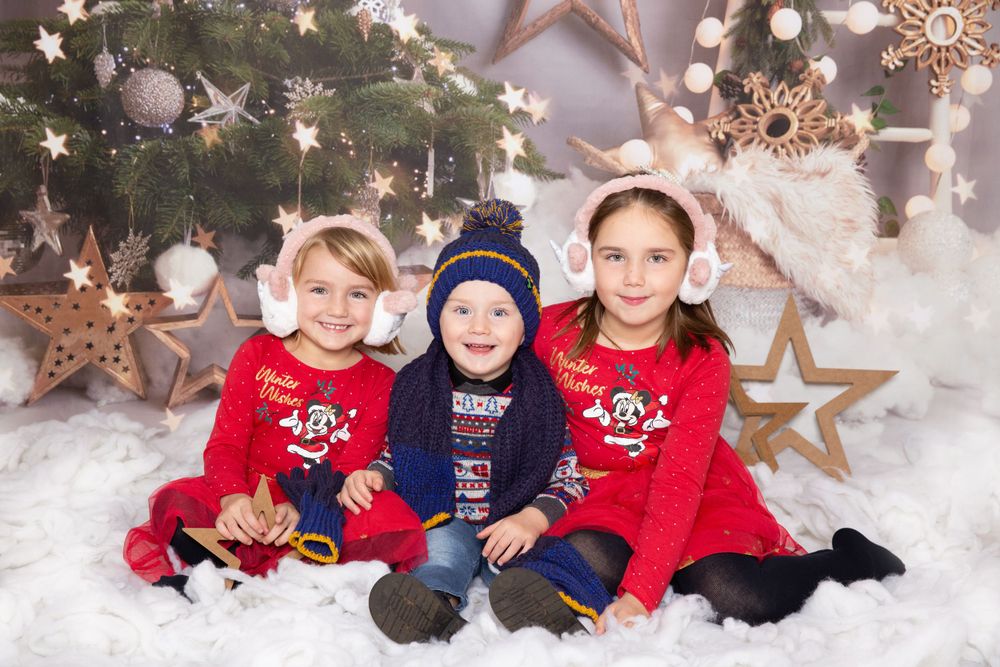 2 children with christmas outfits and hats sat in snow with christmas tree background