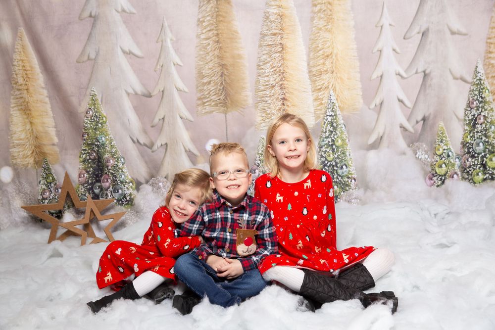 3 children sat in snow with trees in the background