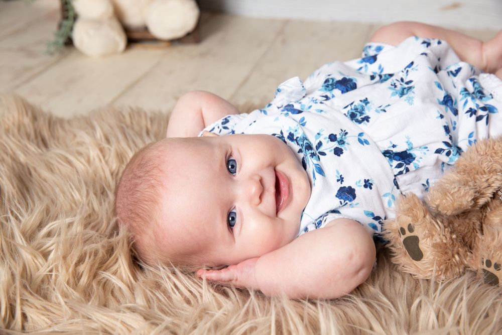 baby laid on flur on fur rug with hands behind her head