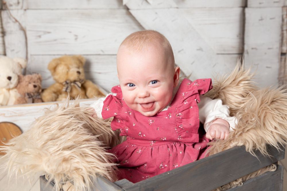 litter baby in pink dress smiling in a grey crate