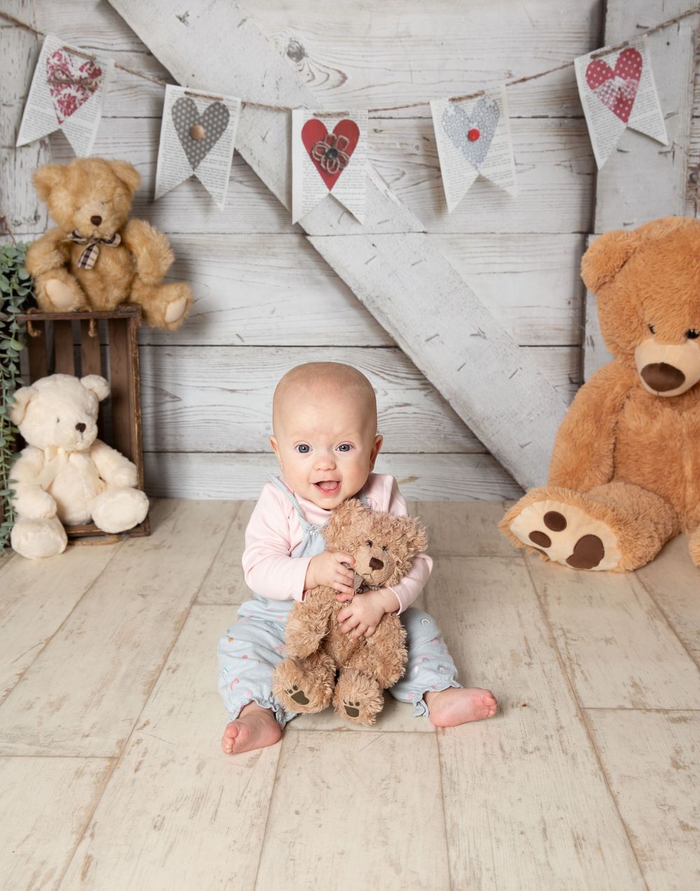 teddies in the background and little baby sat holding a teddy smiling