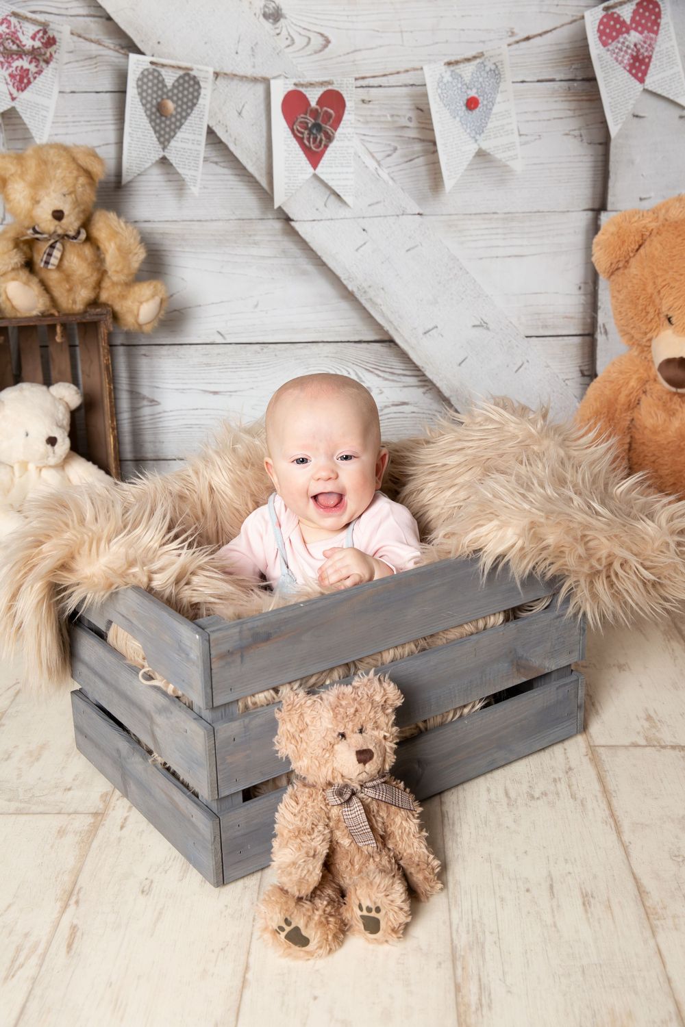 baby smiling sat in a crate with teddy