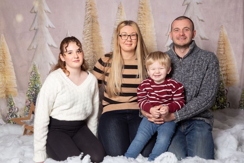 family of 4 sat in snow with trees in the background