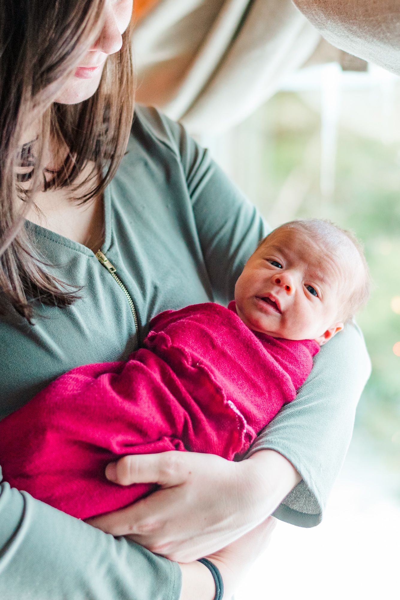 Lifestyle mother holding newborn baby in pink wrap in front of Christmas tree in Pittsburgh, Pennsylvania