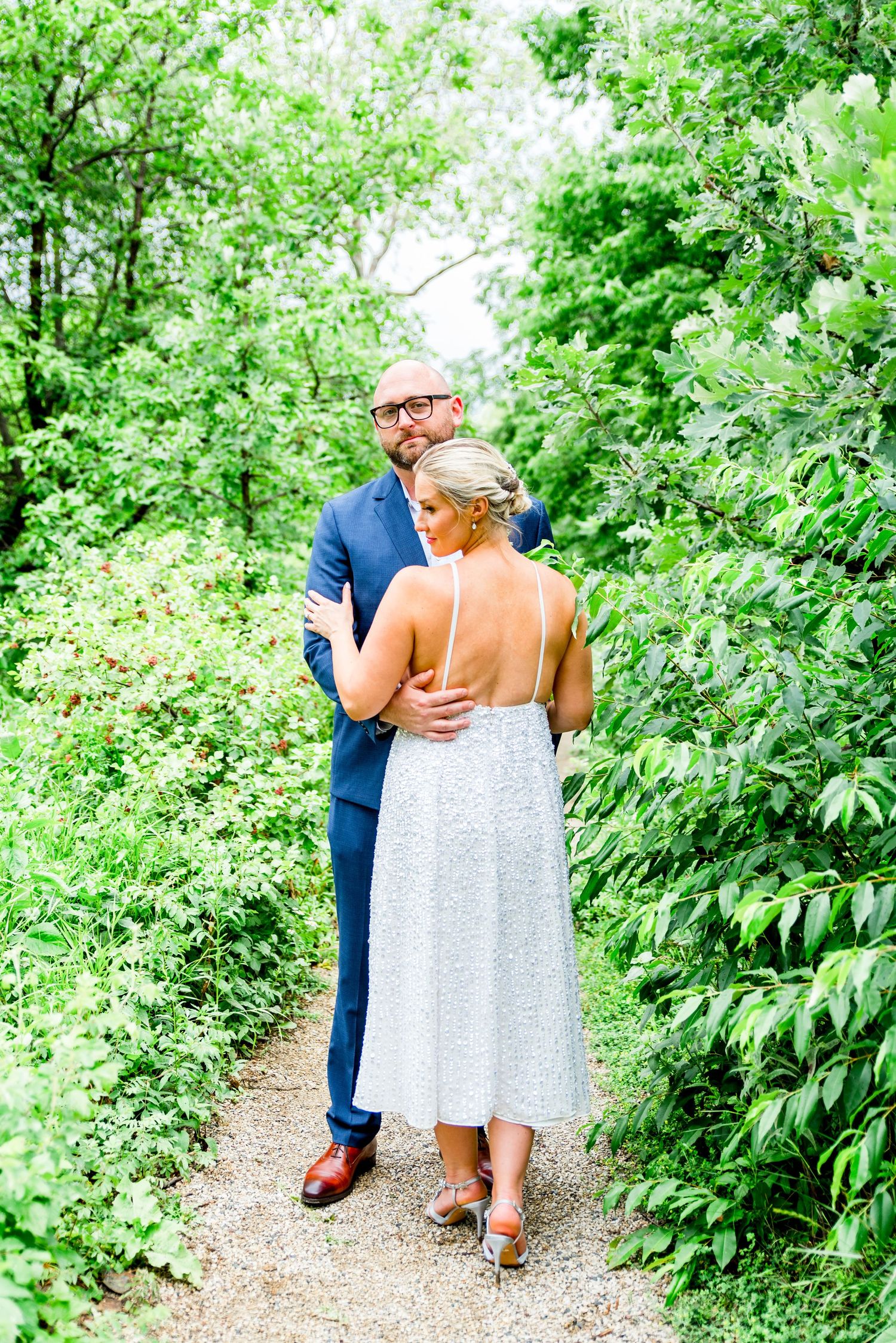 man in navy suit holding blond woman in silver dress at Alfred Caldwell Lily Pool in Lincoln Park