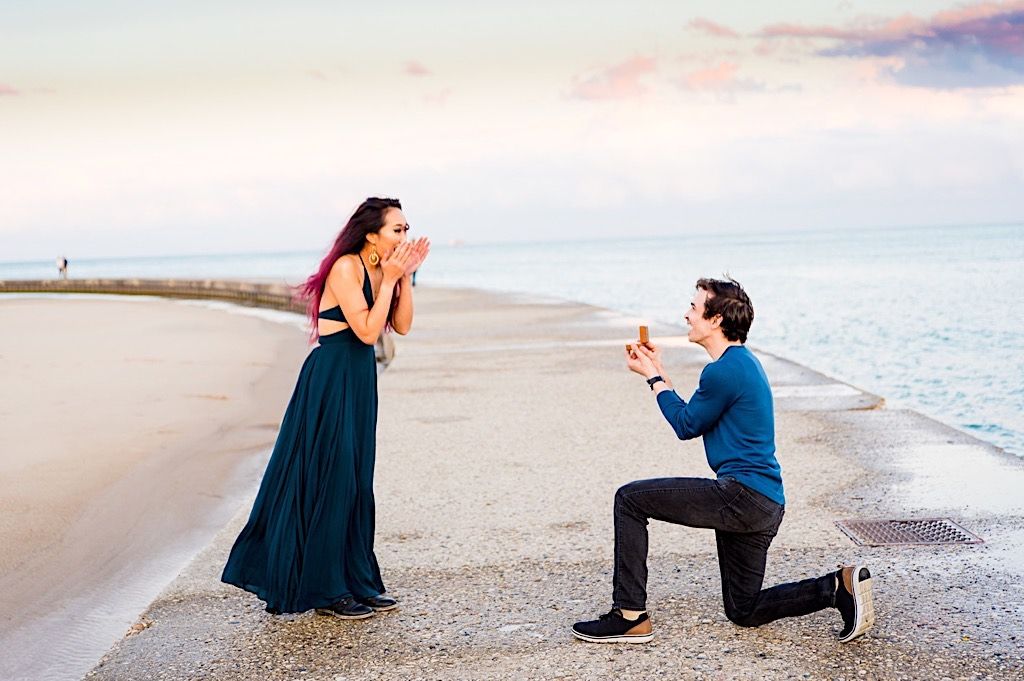 woman in teal dress covering mouth with hands since she's shocked her boyfriend is proposing