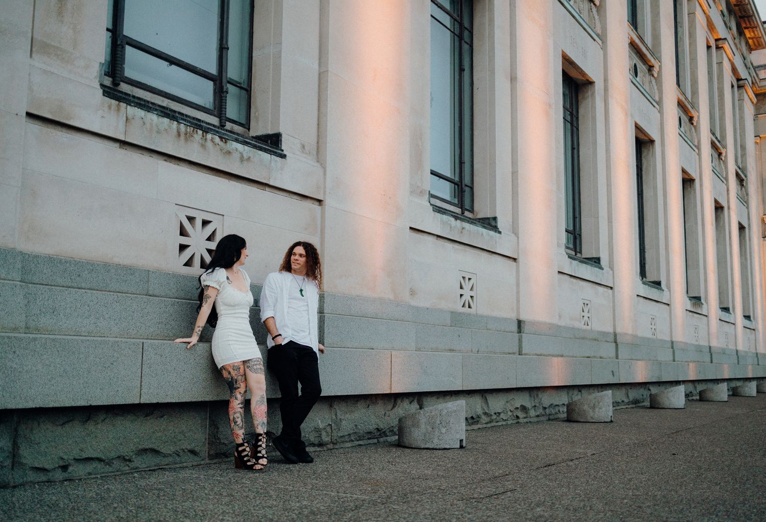 Two people leaning against a building wall at sunset with shadows cast.