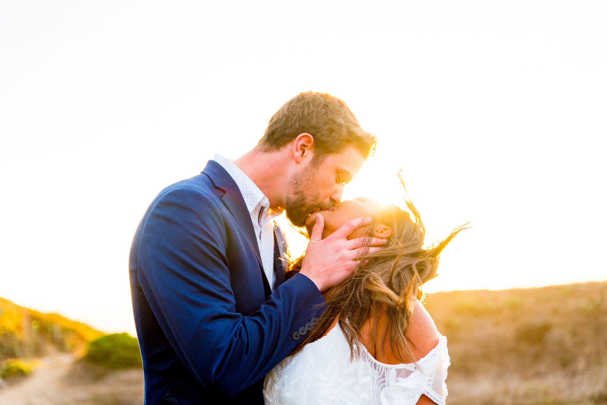 man in blue suit kissing woman in white dress at sunset in San Francisco