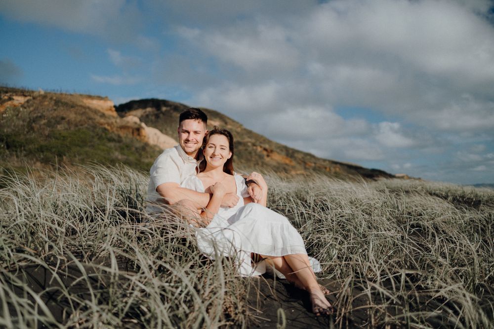Happy couple relaxing together on coastal grass with hills in background.