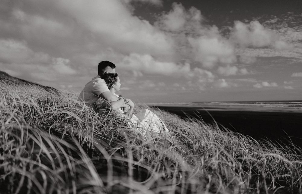 A black and white portrait of a couple embracing in coastal grasslands.