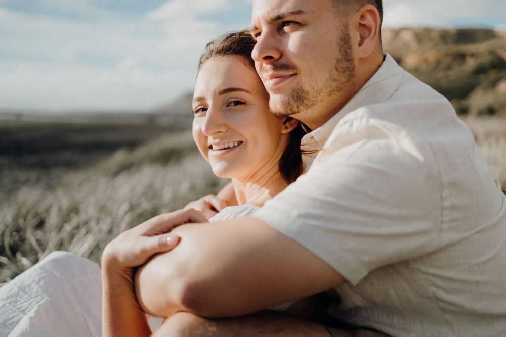 Couple sharing intimate moment on coastal hillside in warm sunlight.
