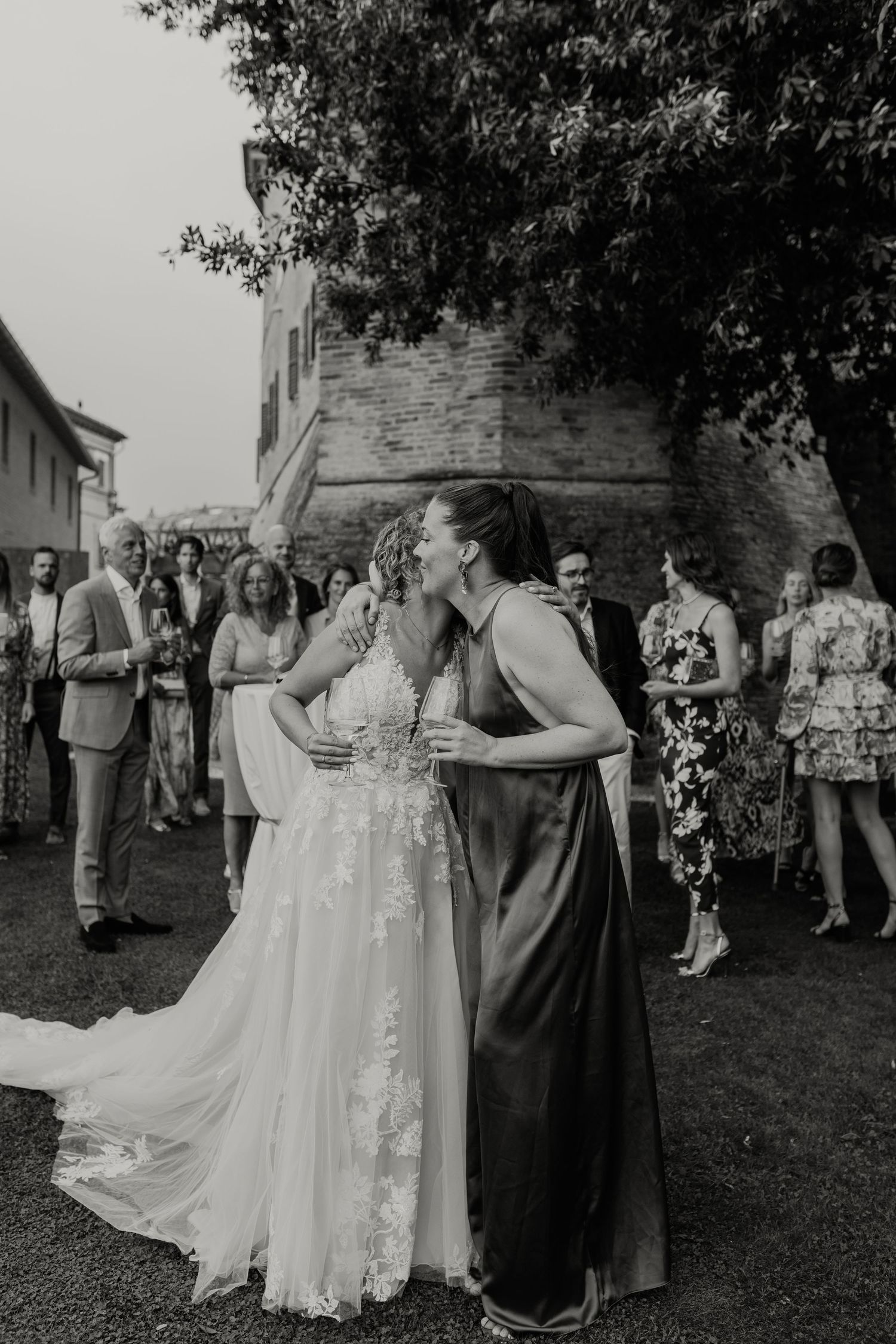 Wedding guests gather outdoors for a celebration near a historic stone building.