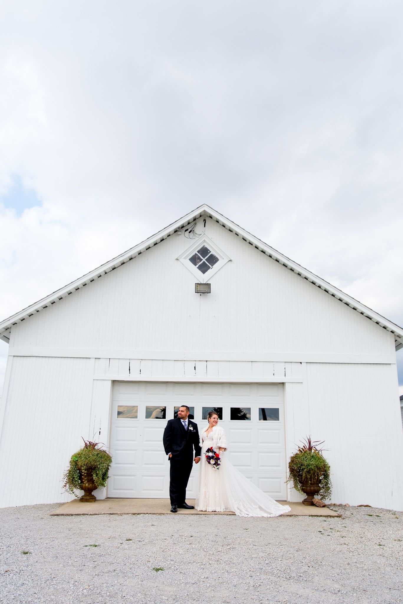 bride and groom holding hands looking in opposite directions in front of a white barn and garage