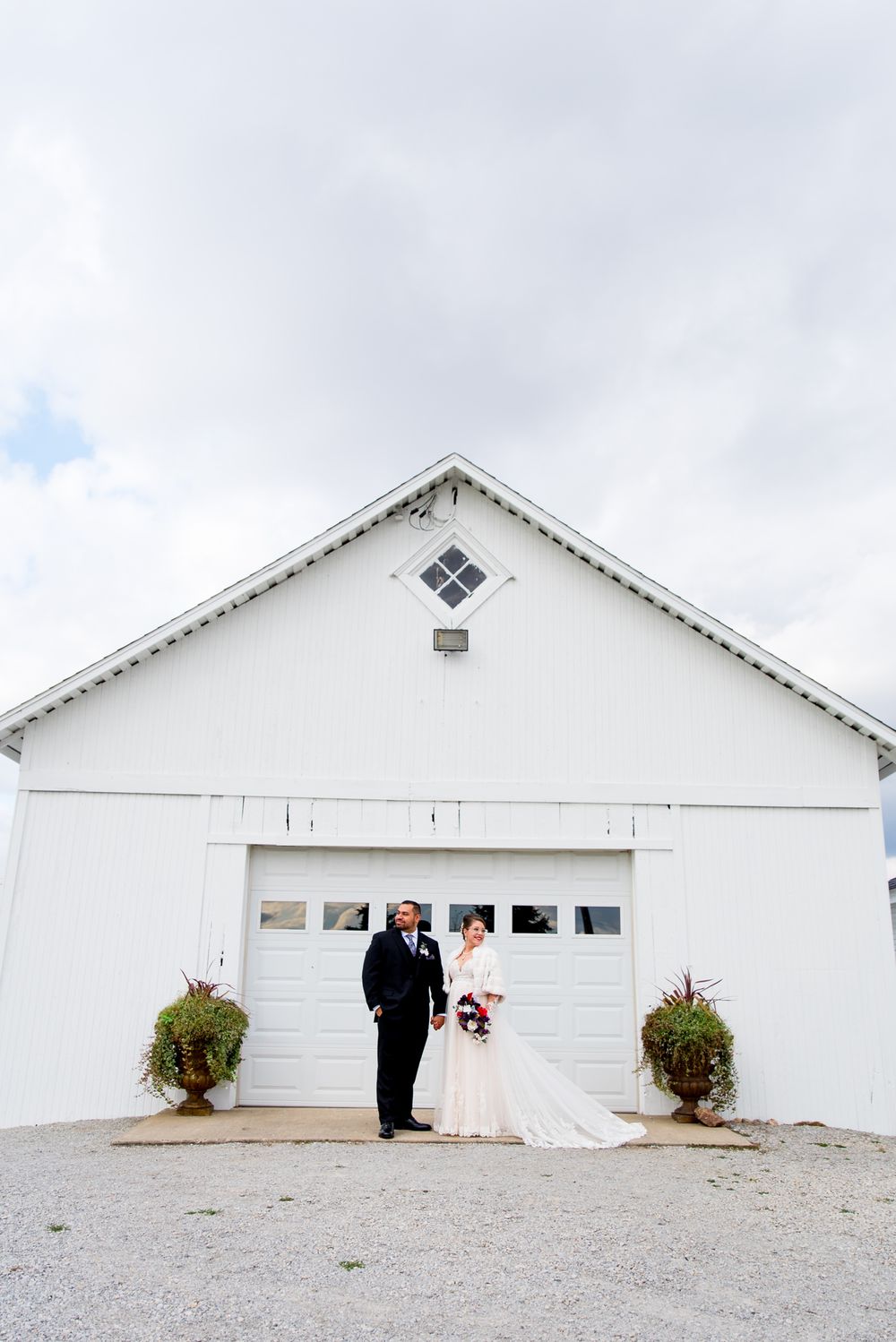 bride and groom holding hands looking in opposite directions in front of a white barn and garage