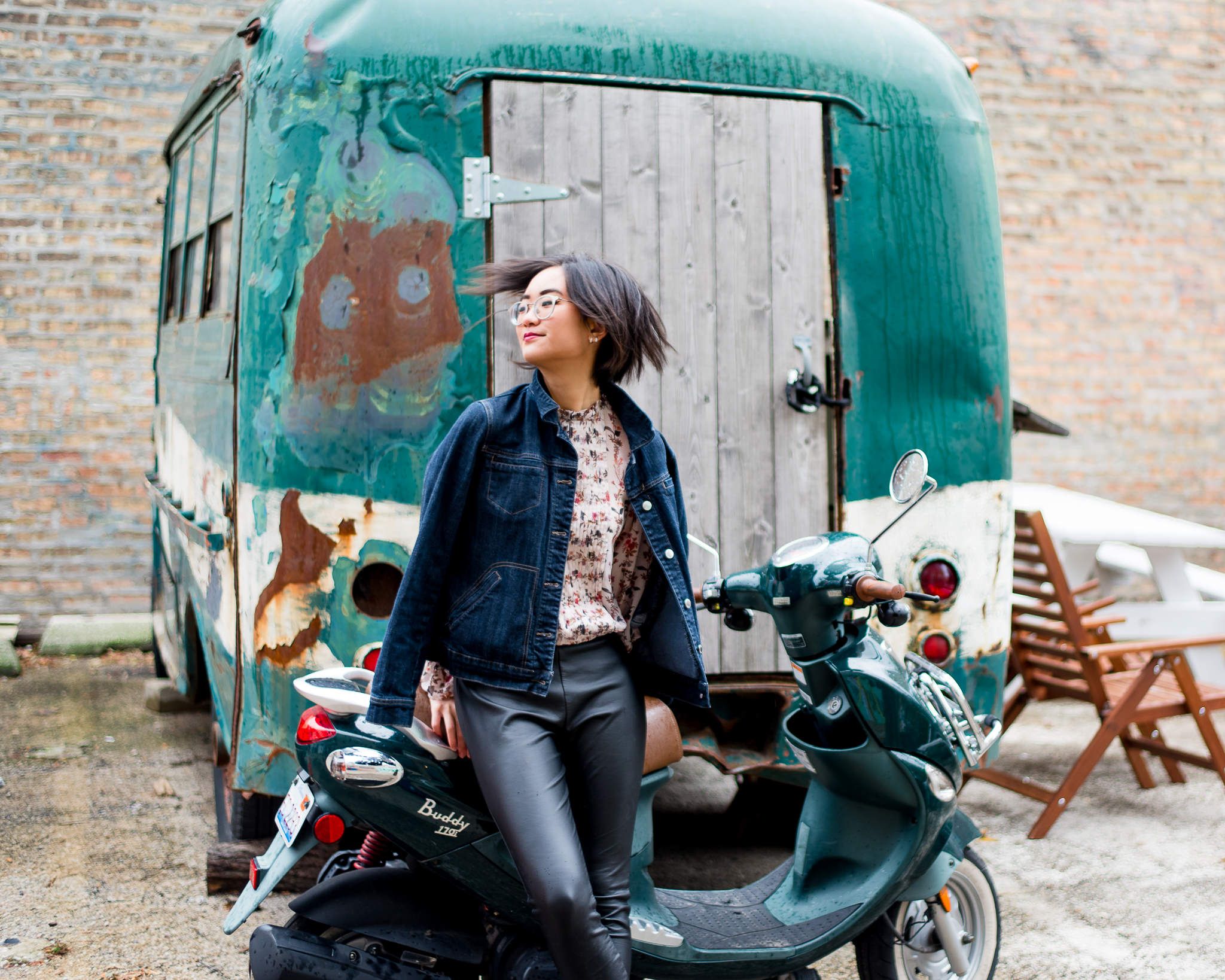 young woman with dark hair in leather pants leaning against teal motorcycle for chicago senior pictures
