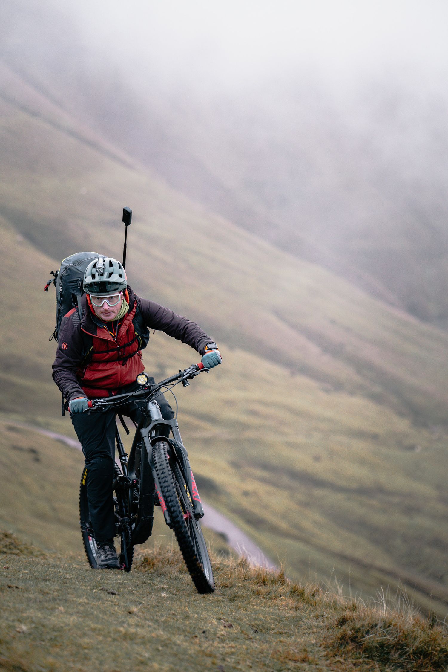A mountain biker rides down a steep dirt trail on rugged mountainous terrain.