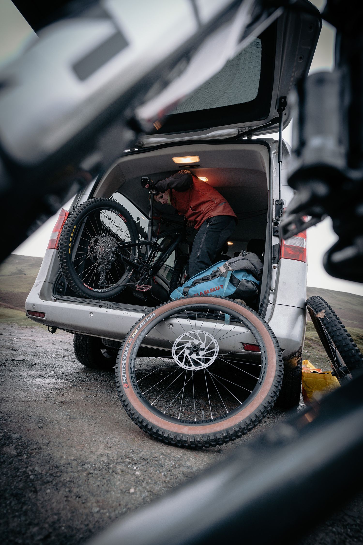 A mountain bike being loaded into the back of a vehicle with gear and equipment.