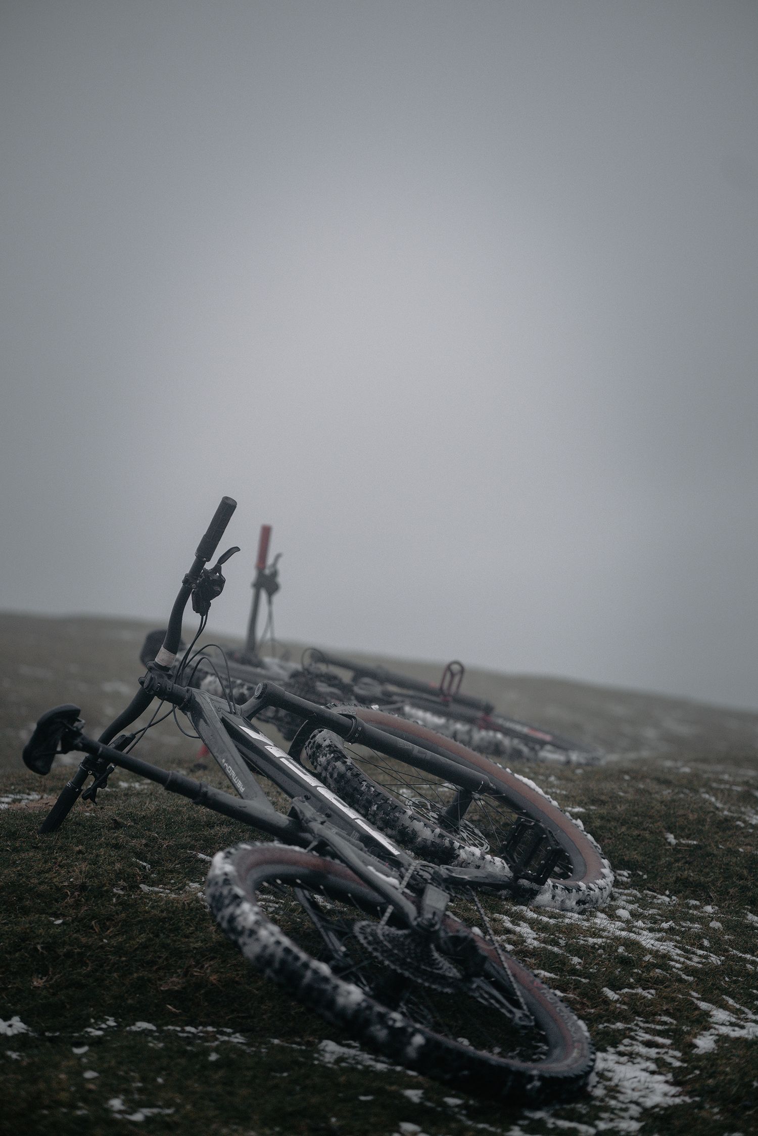 A mountain bike lies on its side on snow-covered ground in foggy conditions.