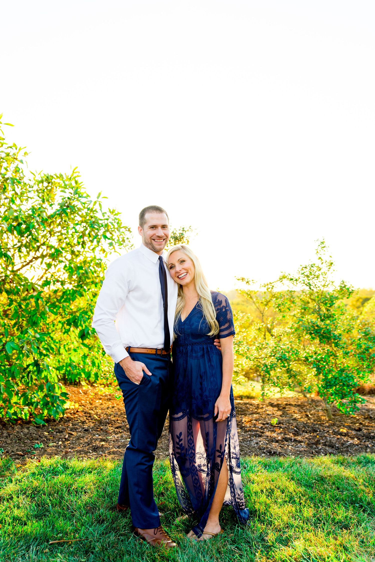 man in white shirt and navy pants holding woman with blonde hair in navy lace dress and smiling at sunset in Grant Park