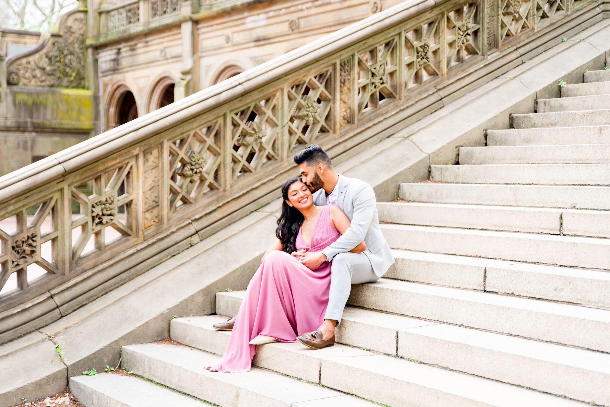 woman in pink dress and man in grey suit sitting on Bethesda Terrace steps and laughing with each other at Central Park