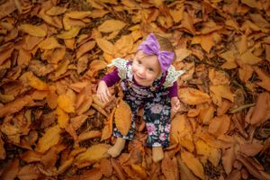 Toddler girl sitting amongst the Autumn leaves by Kate Cashin Photography.