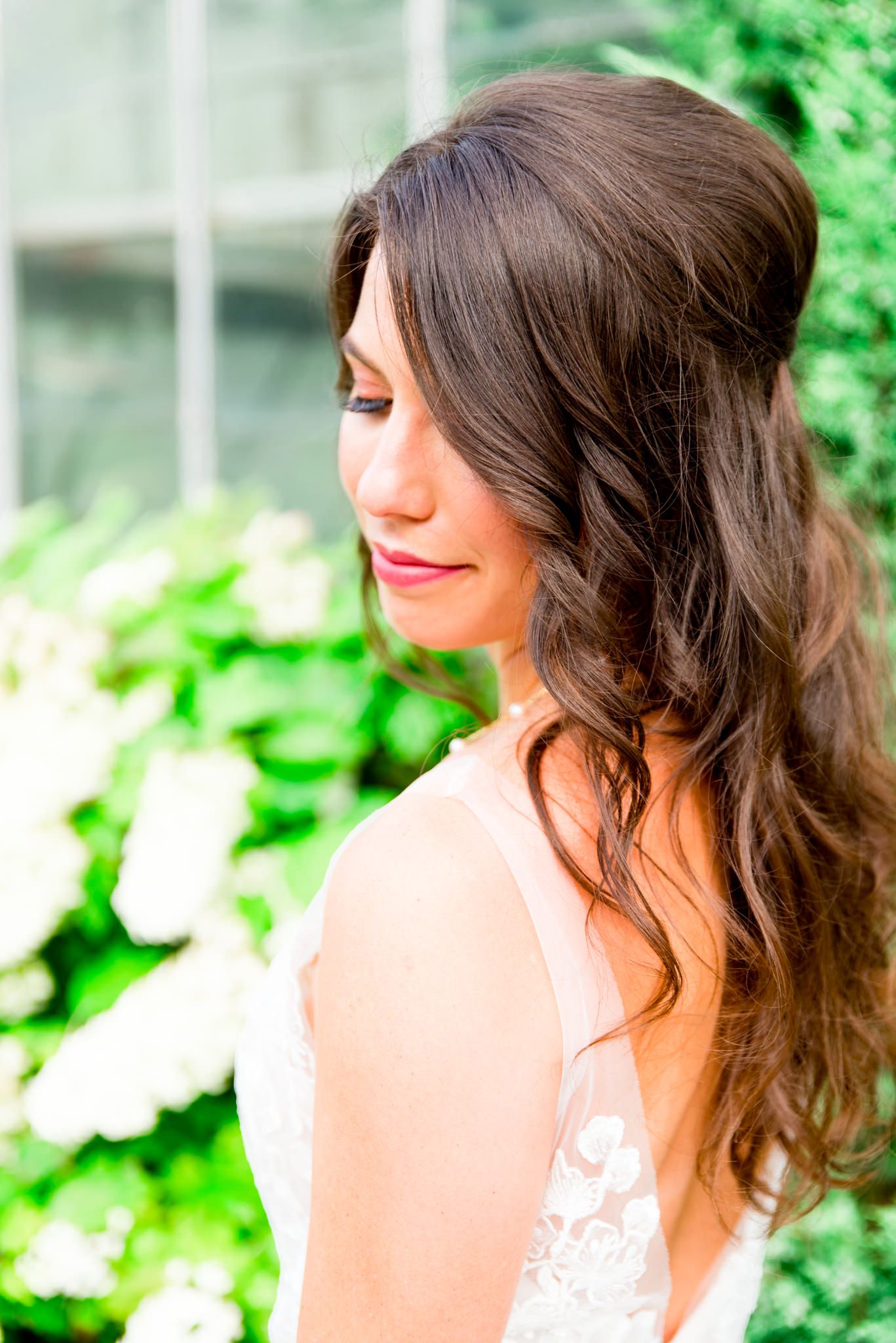 bride with brown hair in loose curls smiling over her shoulder in front of white hydrangea bush at conservatory wedding