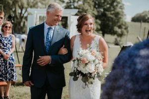 Bride joyously smiling with her dad smiling at her walking down the isle during a wedding in the finger lakes