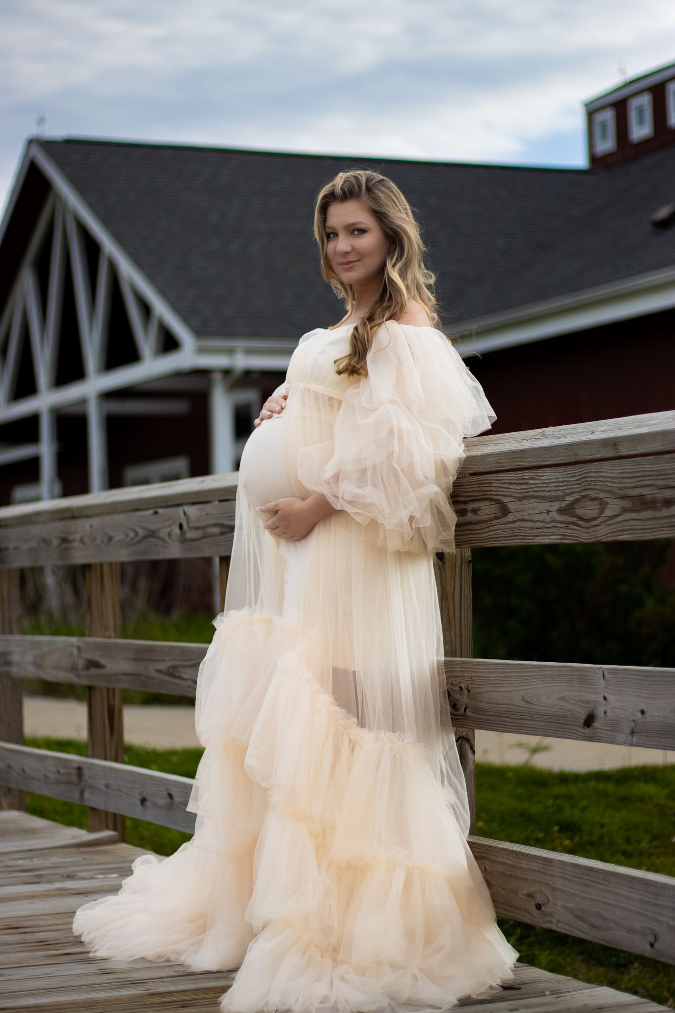 A cream-colored tulle maternity gown photographed against a rustic barn backdrop.