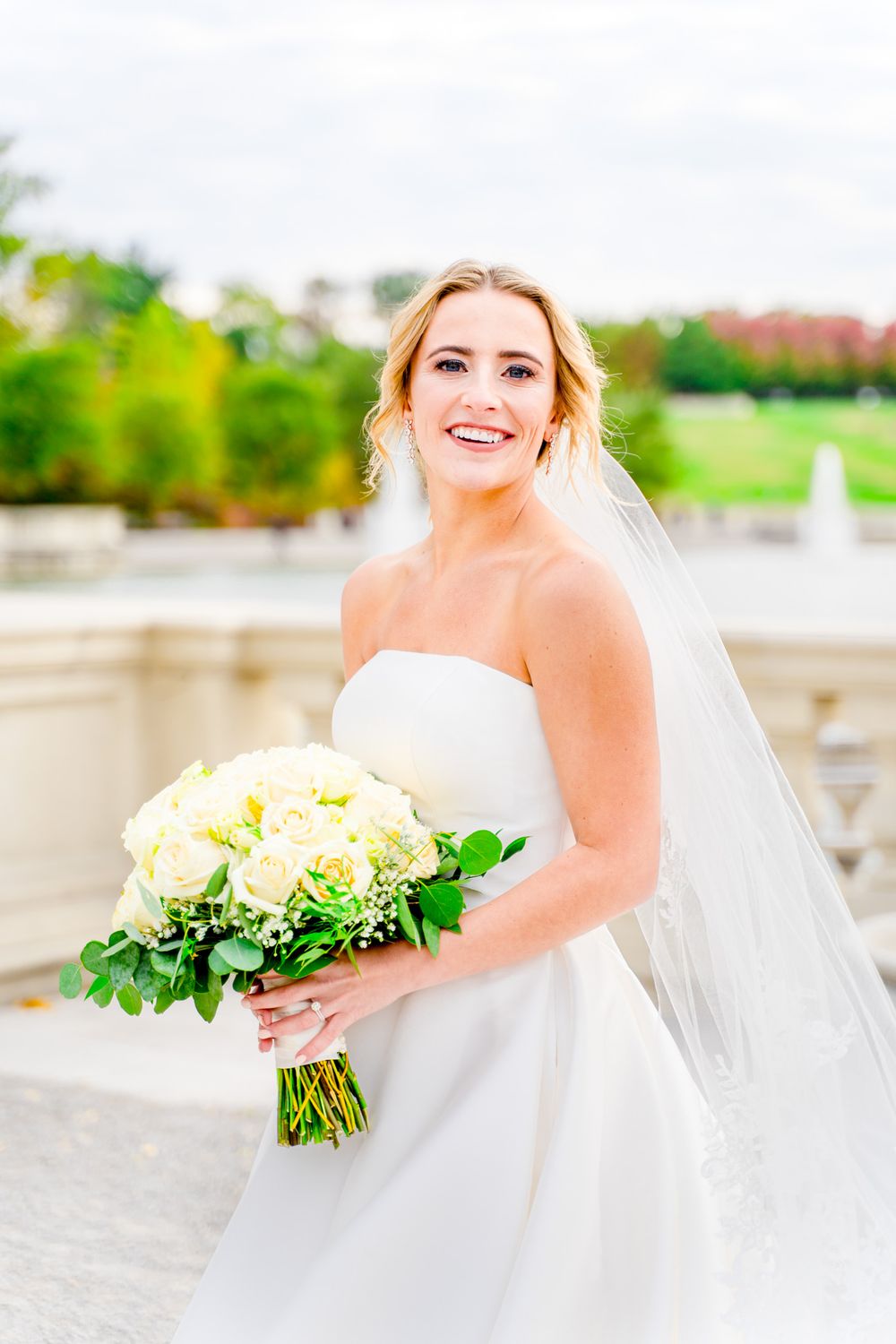 blonde bride with updo and long veil and white bouquet looking over her shoulder in Forest Park wedding pictures