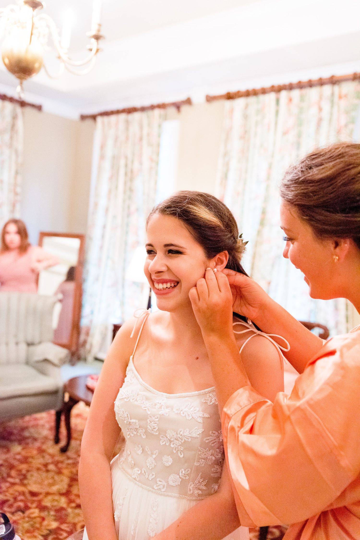 bride smiling while her bridesmaid helps put her earrings on before her wedding in Chicago