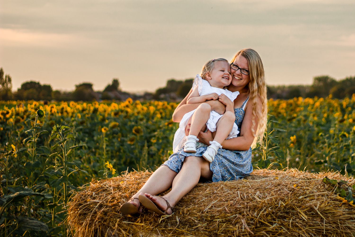 In a sunflower field on Hayling Island a Mum sits on a hay bale laughing with her 2 year old.