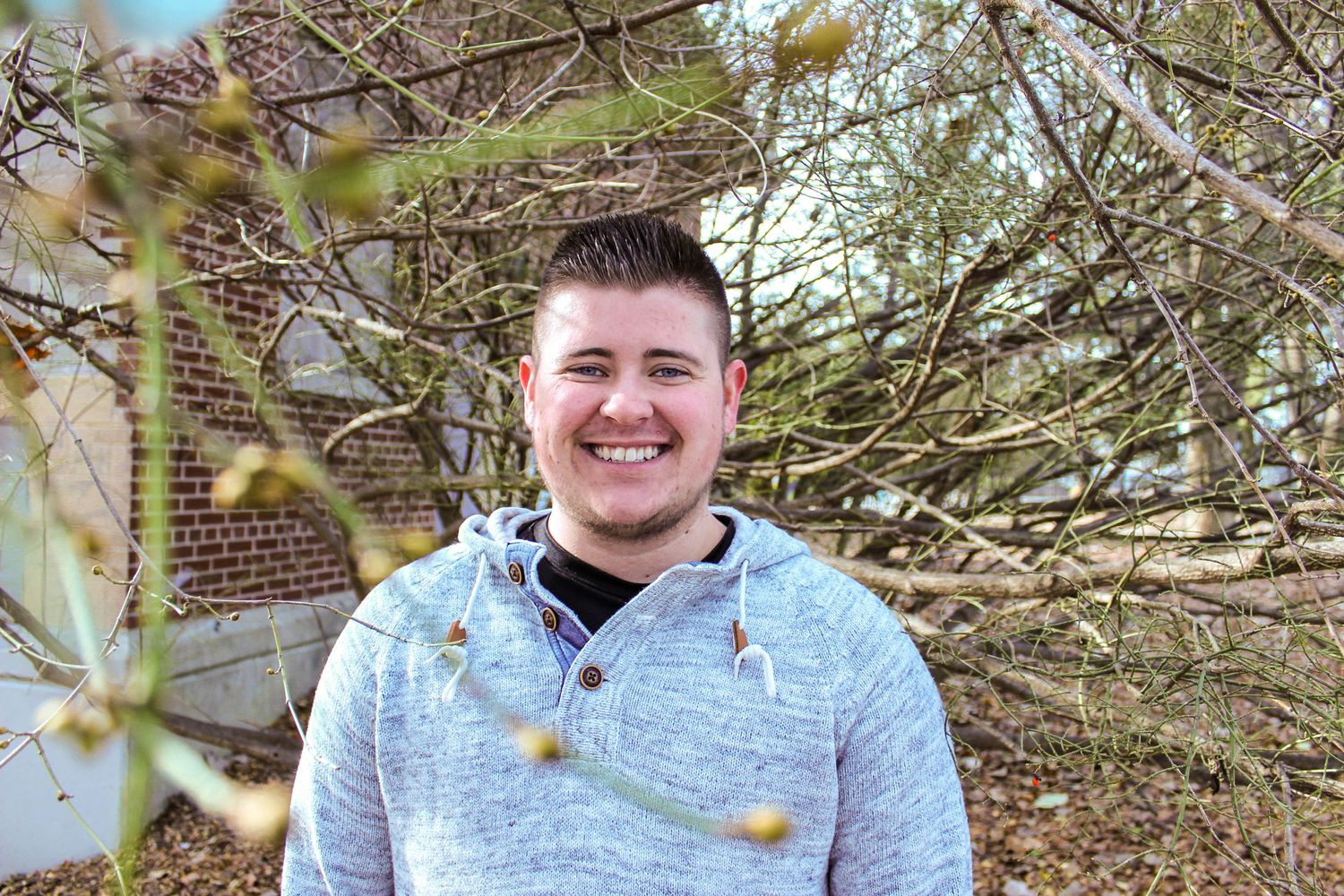 A casual outdoor portrait taken among bare tree branches on a bright day.