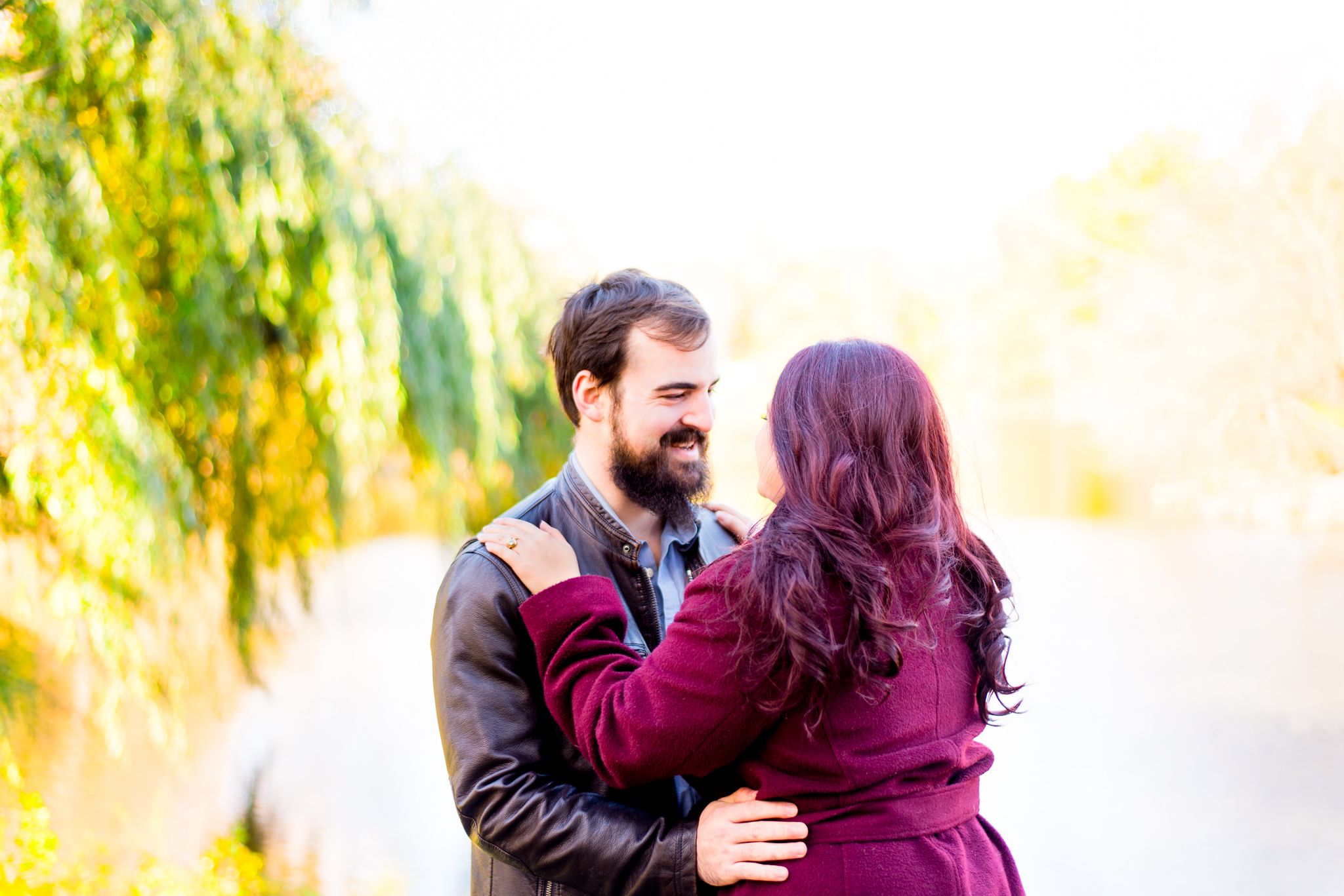 woman with red hair and red jacket hugging brown hair man in brown leather jacket at sunrise in Central Park in the fall