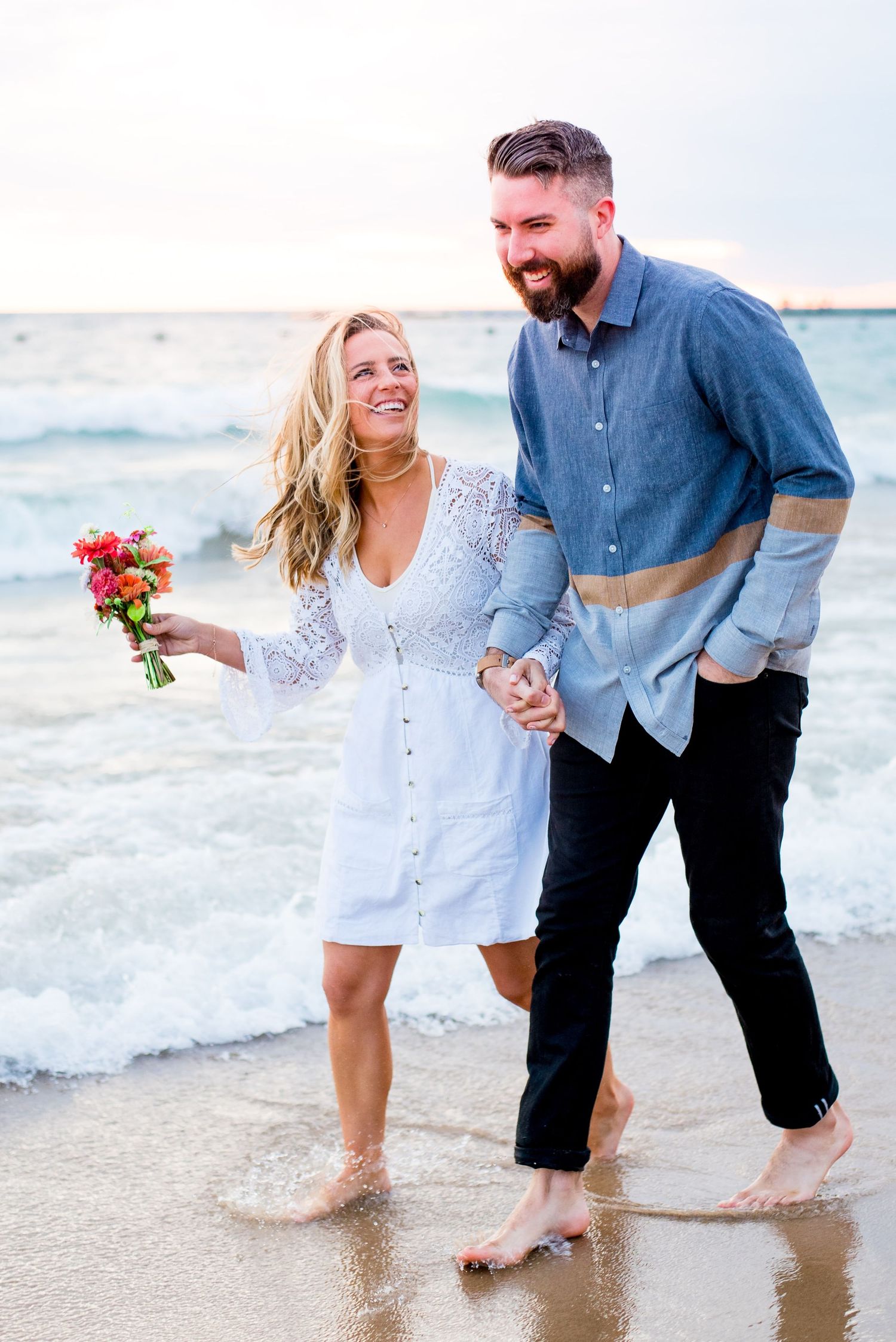 woman in white dress holding hands with dark haired man walking along North Avenue Beach at sunrise