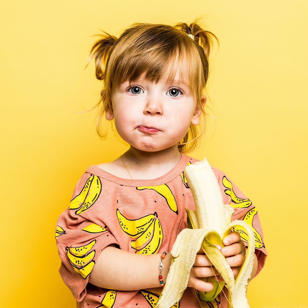 Meisje met banaan in de studio met gele achtergrond