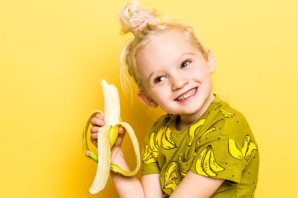 Meisje met banaan in de studio met gele achtergrond