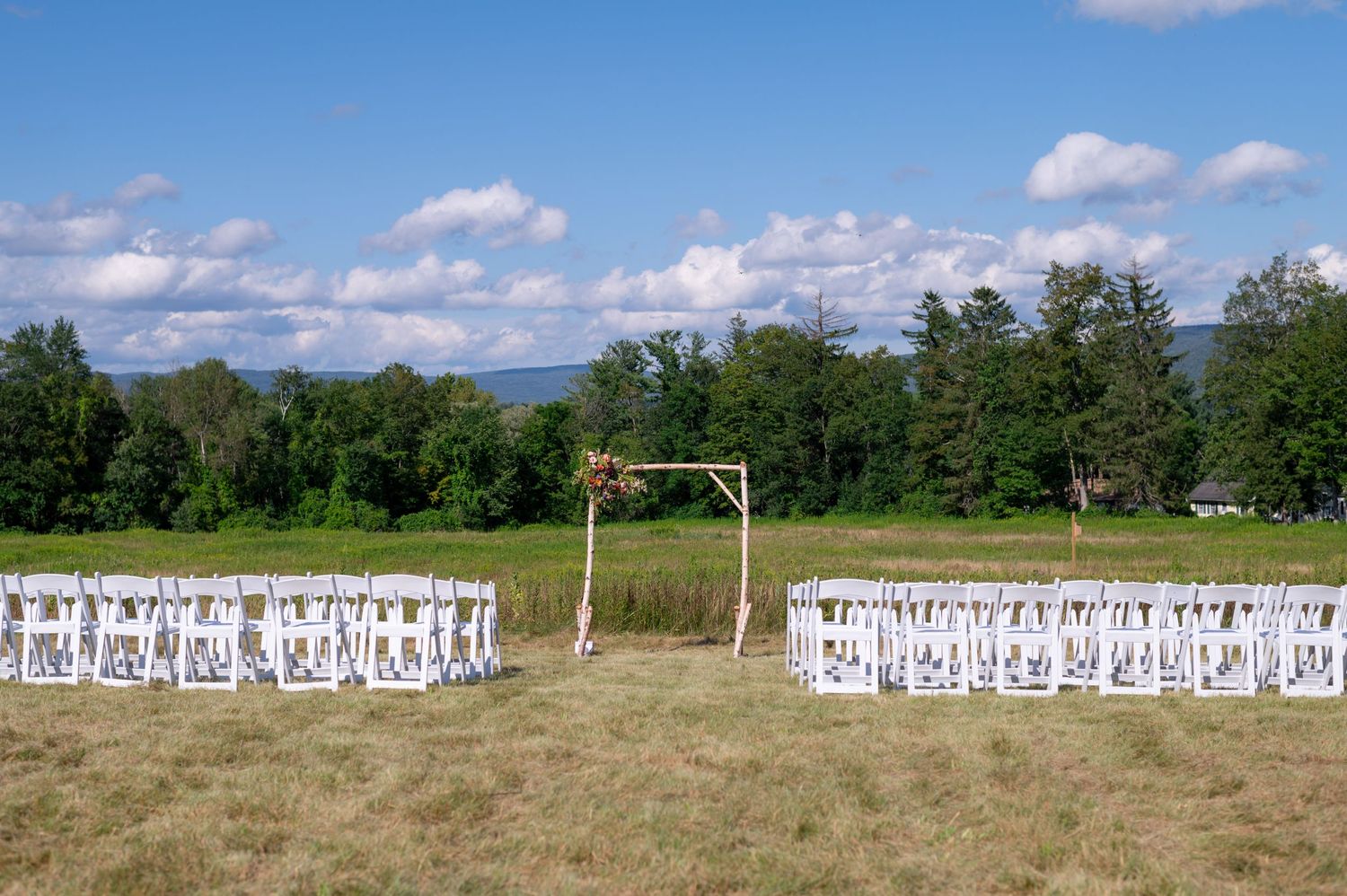 White chairs arranged for an outdoor wedding ceremony with mountains and forest in the background.