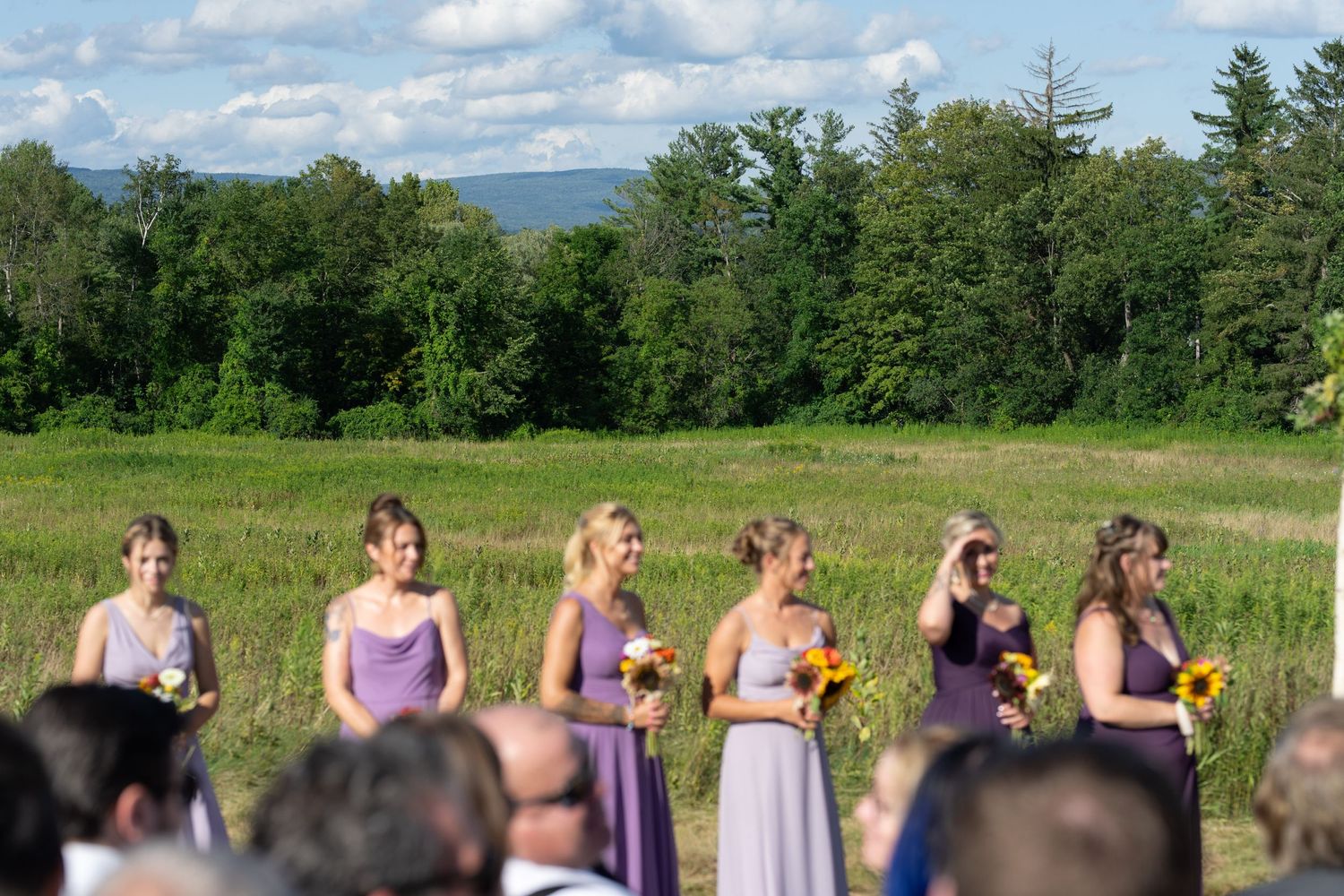Bridesmaids in lavender dresses stand in a row during an outdoor summer wedding ceremony.