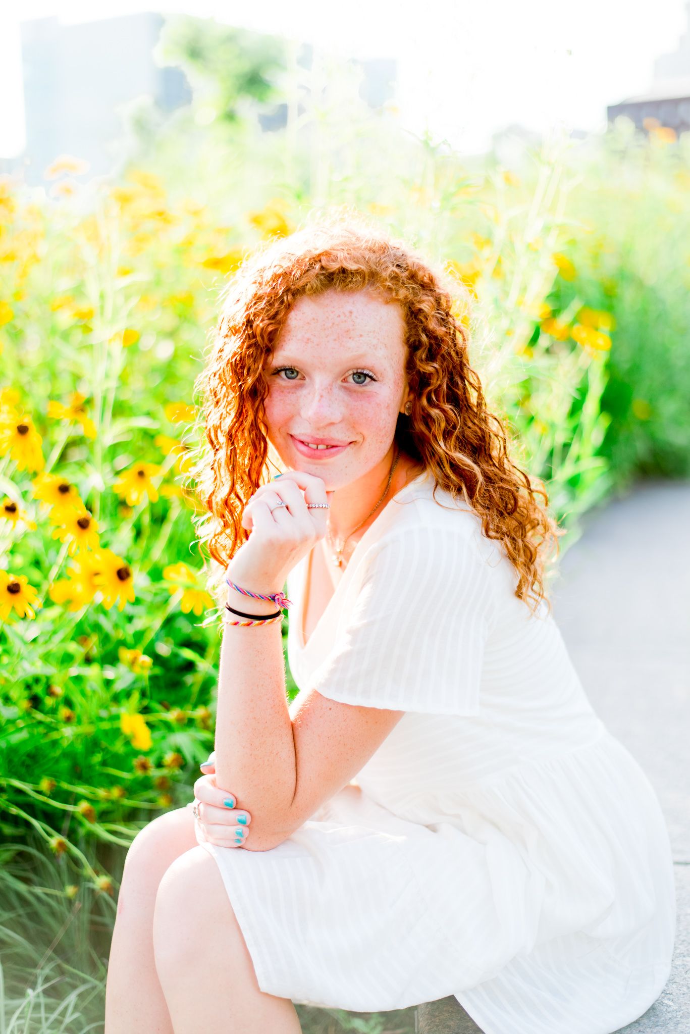 young woman with red curly hair in white dress sitting on concrete bench in front of black eyed susans at Smale Park