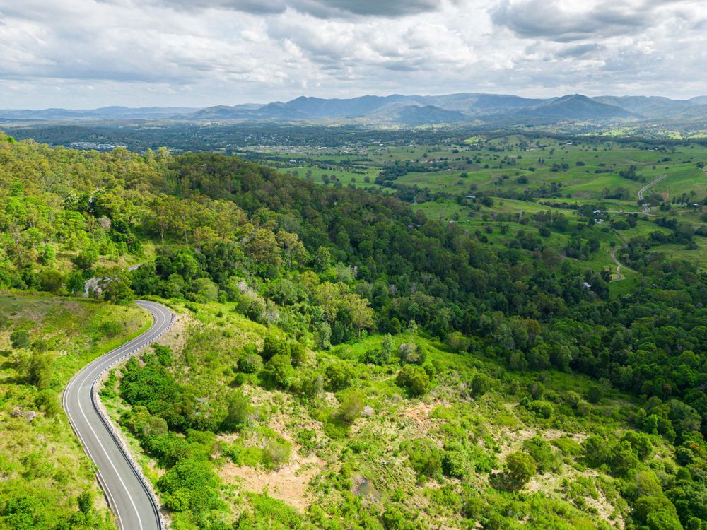Winding mountain road cuts through lush green hills and valleys with distant mountains in view.