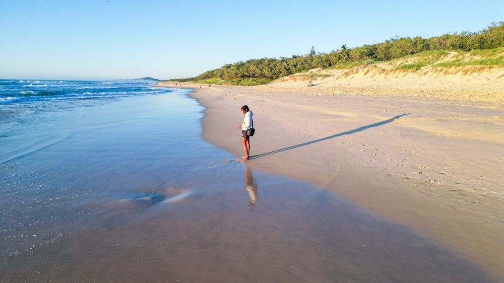 Solitary figure walking along pristine beach shoreline with waves lapping at sandy coast.