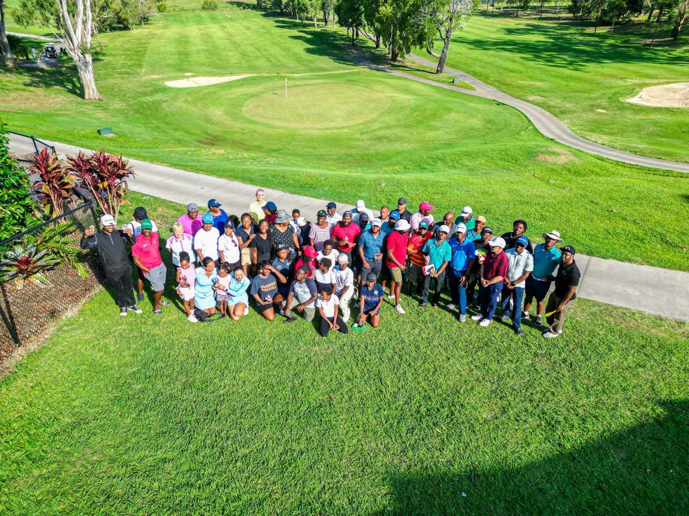 Large group gathered on green hillside of golf course during sunny day.