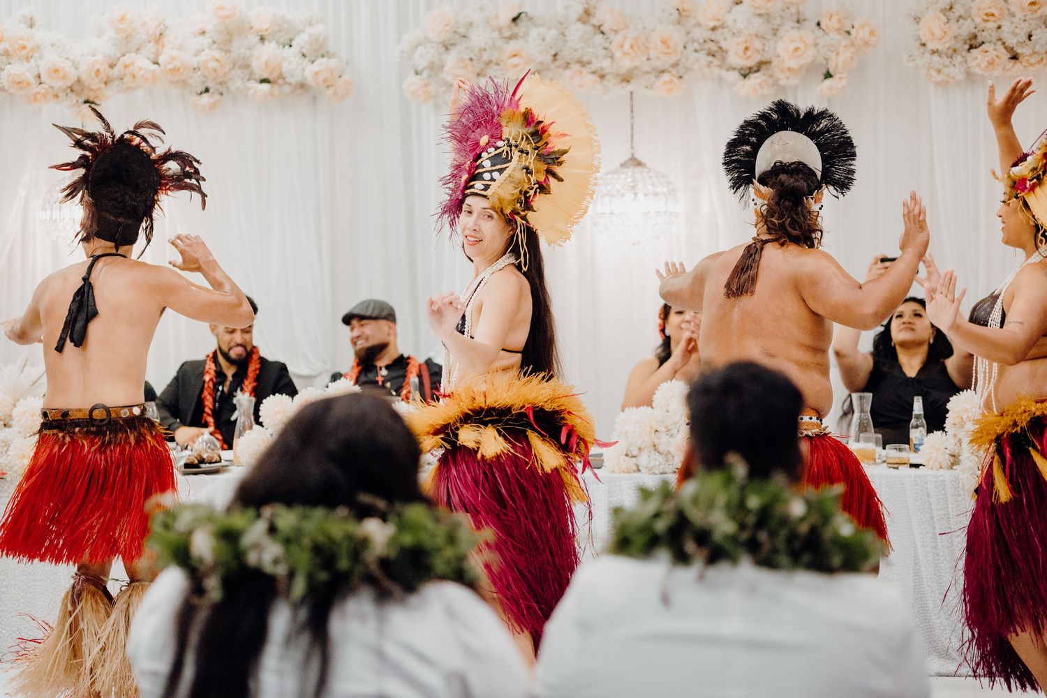 Traditional Polynesian dancers performing in grass skirts at an indoor wedding reception.