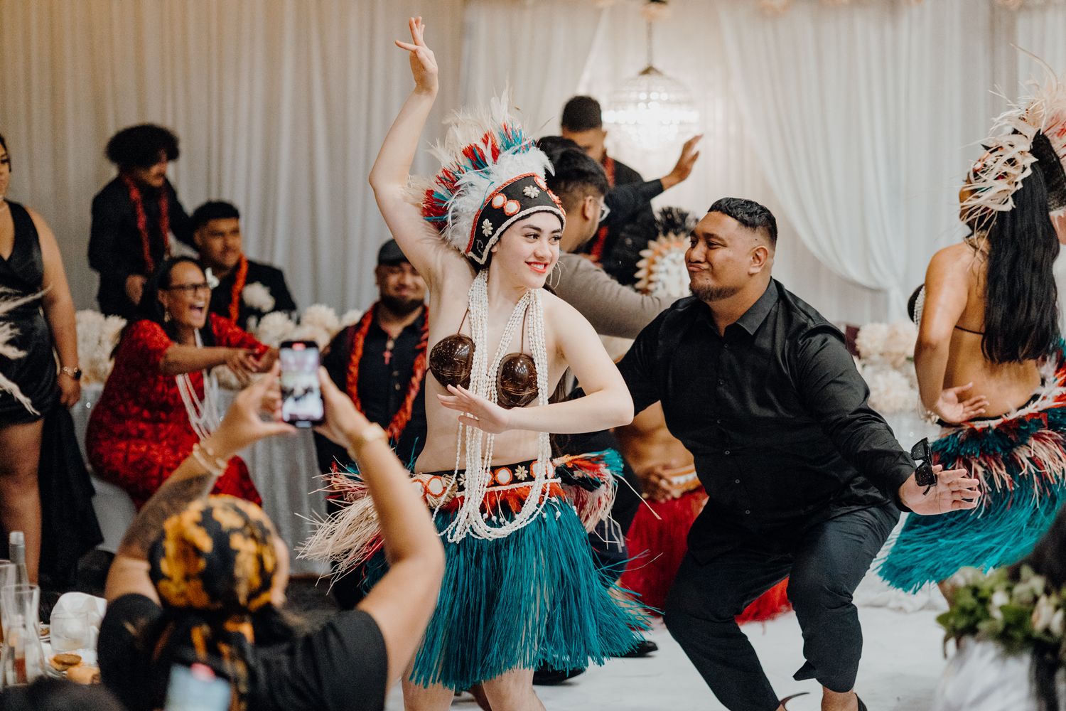 Dancers in grass skirts and traditional attire performing choreographed moves at a wedding reception.