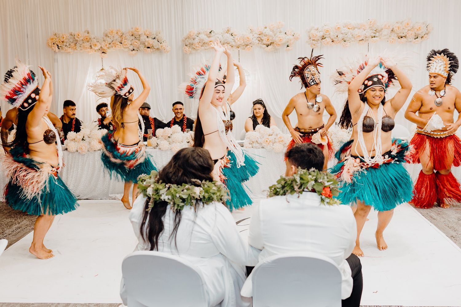 Group of dancers in traditional Polynesian attire performing synchronized moves at indoor celebration.