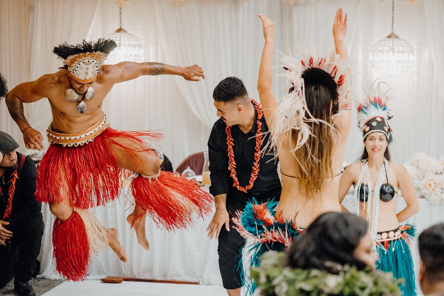 Energetic Polynesian dance performance with dancers in traditional costumes at an indoor celebration.