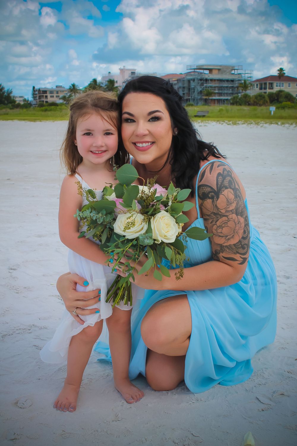 A beach portrait with bouquet of white roses against coastal buildings in background.