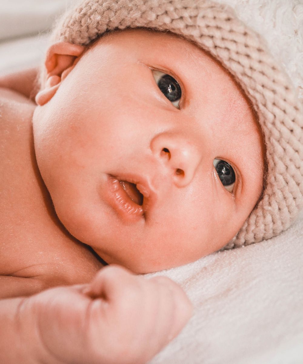 A baby wearing a knit beanie gazes at the camera with wide eyes.